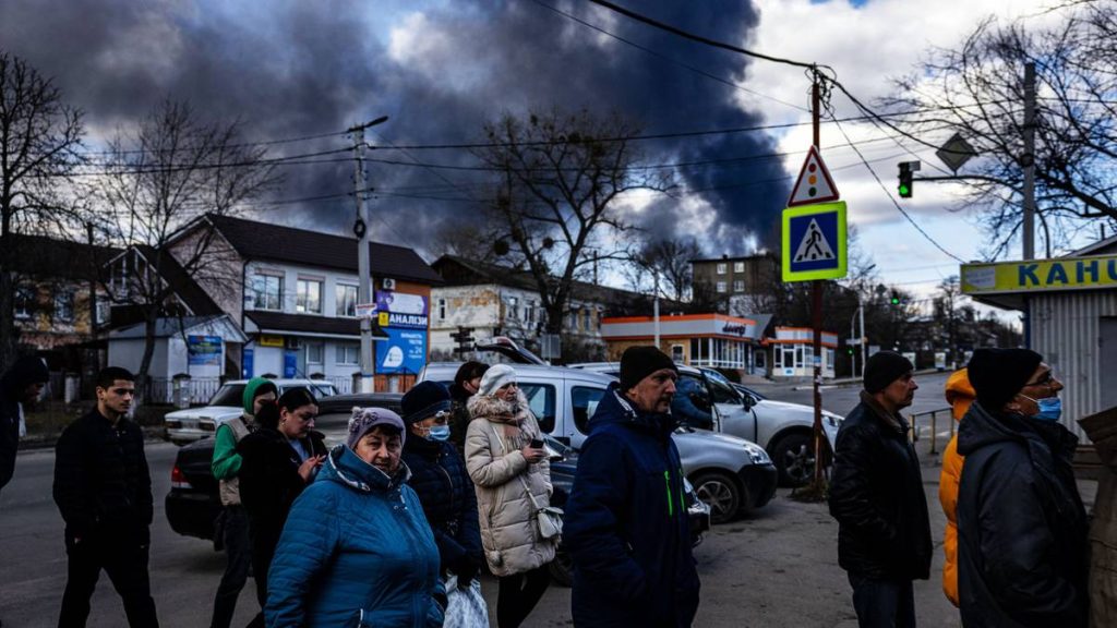 Innbyggere i Kyiv-forstaden Vasylkiv sto i kø for å skaffe mat søndag mens det røyk fra eksplosjoner steg opp i bakgrunnen.