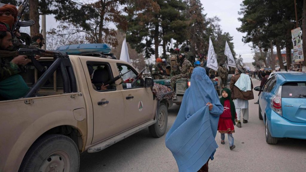 En burka-kledd kvinne går forbi Taliban-krigere i under en parade i Maymana i januar i år.