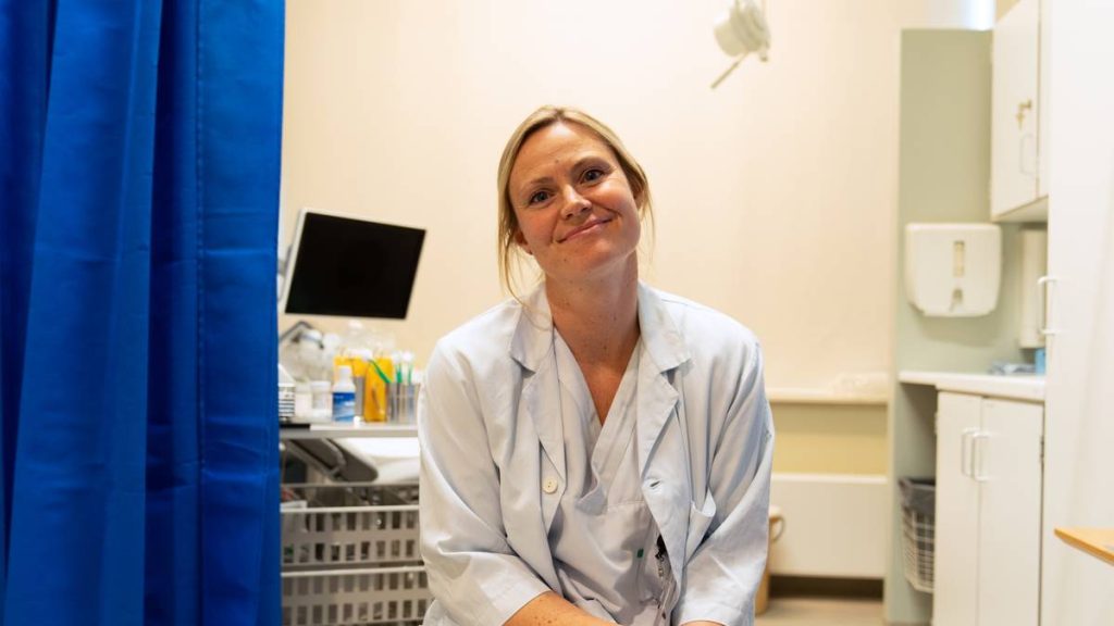 Overlege Camilla Kleveland sitter i et hvitt sykehusrom på St. Olavs Hospital i Trondheim. Hun har på seg legefrakk og ser inn i kamera.
