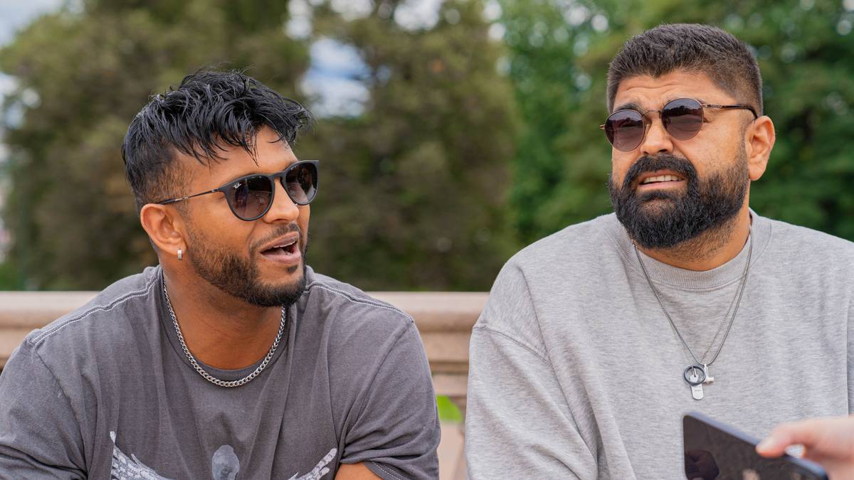 To menn med solbriller sit på ein benk og blir intervjua av ein reporter